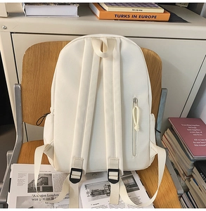 Detail view of cream-white canvas backpack featuring padded straps and a side zipper pocket