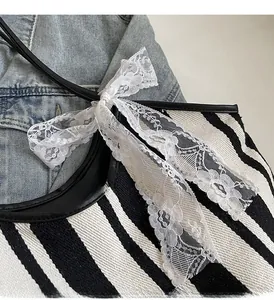 Close-up of black and white striped canvas tote with a white lace bow and leather strap