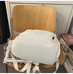 Detail of a minimalist cream-colored nylon backpack featuring a large zipper pocket
