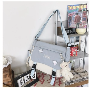 Close-up of light blue and beige messenger bag with buckle and plush bear pendant
