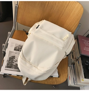 Detail view of a cream minimalist backpack with drawstring side pockets on a chair