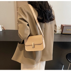Chic beige crossbody bag with gold turn-lock closure worn by a model in a café