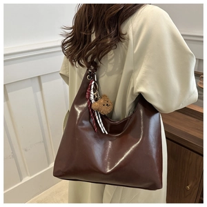 Detail view of large coffee brown tote bag with bear charm and ribbon on model's shoulder