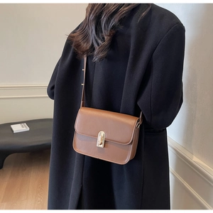 Classic brown leather square crossbody bag with gold push-lock worn on a black coat