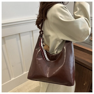 Detail view of dark brown semi-moon tote with shoulder knot and plush bear charm