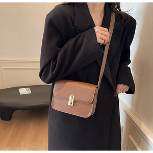 Minimalist brown square crossbody bag with gold metal clasp on a black coat outfit
