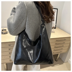 Detail of a black glossy leather hobo bag with slim straps worn as a shoulder bag