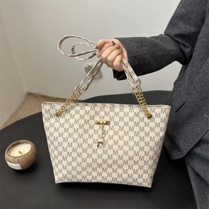 Schicke beige Tragetasche mit M-Print und goldener Kette in der Hand gehalten