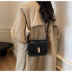 Minimalist black square crossbody bag with gold buckle on a model in a trench coat