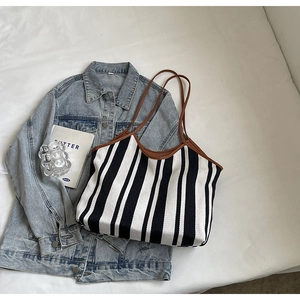 Close-up of striped canvas tote bag with brown leather handles and denim jacket detail