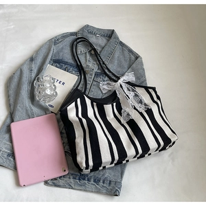 Close-up of striped canvas tote bag featuring an elegant white lace bow and leather handles