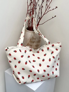 Detail of a white strawberry print nylon tote bag with durable handles on a minimalist stand