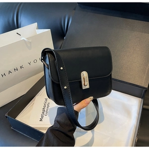 Detail of minimalist black leather square bag with elegant gold metal push-lock clasp