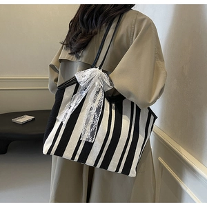 Close-up of a striped canvas tote bag with a white lace bow detail and slim black straps