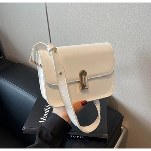 Close-up of a white minimalist flap bag featuring a prominent gold U-shaped twist lock