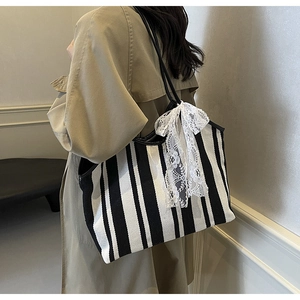 Detail of striped canvas tote bag with a white lace bow accessory on a model