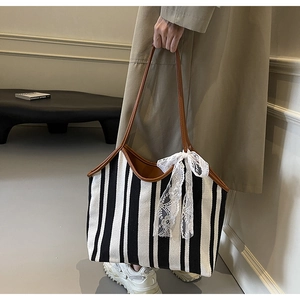 Macro shot of striped canvas tote bag with brown leather trim and white lace bow detail