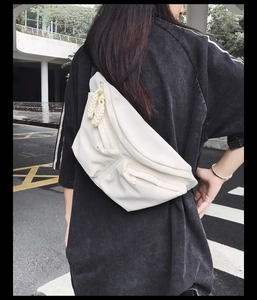Close-up of off-white multi-pocket nylon crossbody bag with woven rope zipper pulls