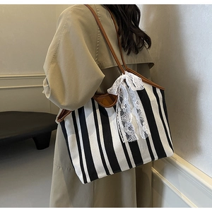 Detail of canvas tote bag with black and white stripes and large white lace bow accent