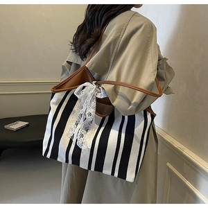 Close-up of striped canvas tote bag featuring brown leather trim and a white lace ribbon