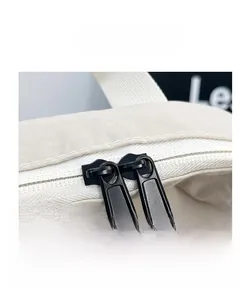 Detail view of the durable dual matte black zipper closure on an ivory nylon backpack