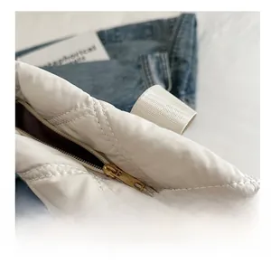 Detail of a white quilted tote bag featuring smooth gold metal zipper closure and webbing handle