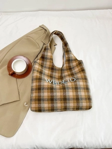 Detail of vintage plaid wool tote bag with embroidered letters on a textured surface