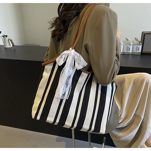 Close-up of striped canvas tote bag with brown leather handles and a white lace bow detail