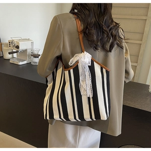 Close-up of striped canvas tote bag with brown leather handles and lace bow detail