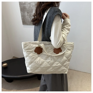 Detail of white quilted tote bag featuring brown floral leather patches and shoulder strap