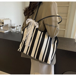 Detail of striped canvas tote bag with white lace bow and black shoulder straps