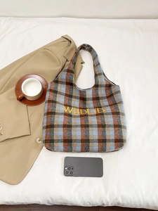 Flat lay of plaid wool tote bag with yellow embroidery on white bedding with accessories