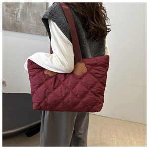 Detail of burgundy quilted tote bag featuring leather flower patches on the shoulder strap