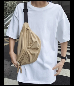 Outdoor street view of a khaki utility crossbody chest bag with adjustable black strap