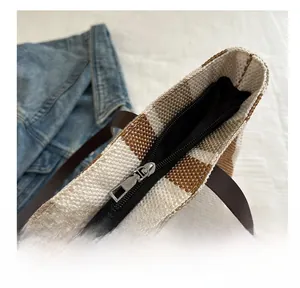 Detail of the smooth silver zipper closure on a brown checkered woven tote bag