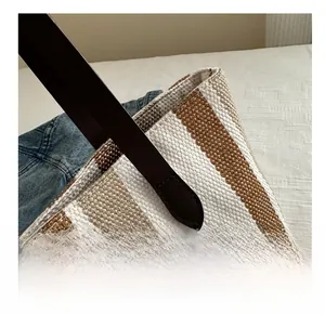 Macro shot of striped woven tote bag handle with refined dark brown leather stitching