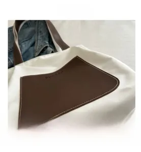 Detail showing the brown leather pocket and logo on the white minimalist tote bag