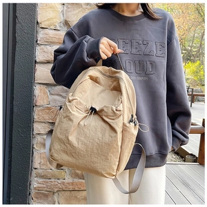 Detail of beige nylon backpack featuring drawstring closure and functional side pockets