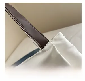 Detail view of precise stitching and premium brown leather handle on a white tote bag