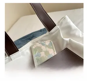 Detail of the white canvas tote bag featuring a brown leather front pocket with white stitching