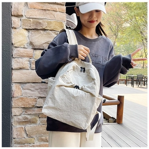 Detailed outdoor view of a cream canvas backpack featuring functional drawstring pockets