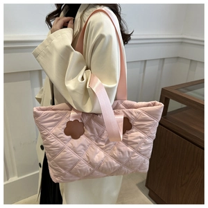 Detail of light pink quilted tote bag featuring floral leather patches and wide straps