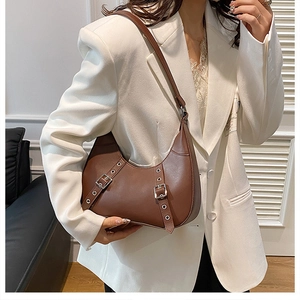 Braune Crescent-Tasche aus Leder mit Metallschnallen an Modell in weißem Anzug gezeigt