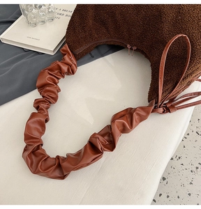 Detailed view of brown plush dumpling bag featuring ruched faux leather strap and dual zippers