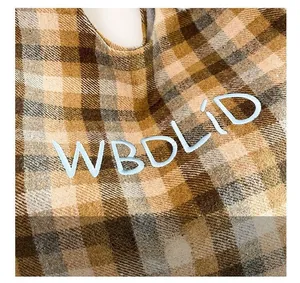 Detailed close-up of brown plaid wool fabric featuring blue embroidered WBDLID text