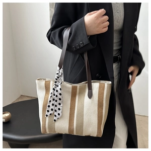 Detail of canvas tote bag with vertical stripes and silk scarf on shoulder strap