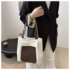 Detail of the leather front pocket with embossed logo on a cream canvas tote bag