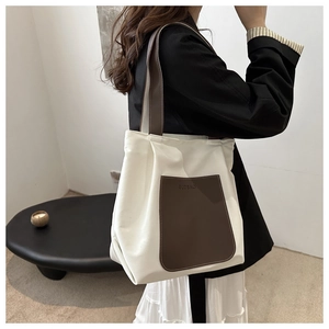 Detailed close-up of a cream canvas tote bag with a brown leather pocket and strap detail