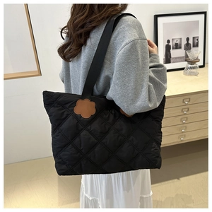 Detail of black quilted tote bag featuring unique brown floral charms on shoulder straps