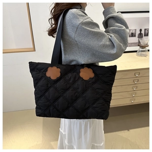 Close-up of black quilted tote bag with brown floral leather patches on the shoulder strap